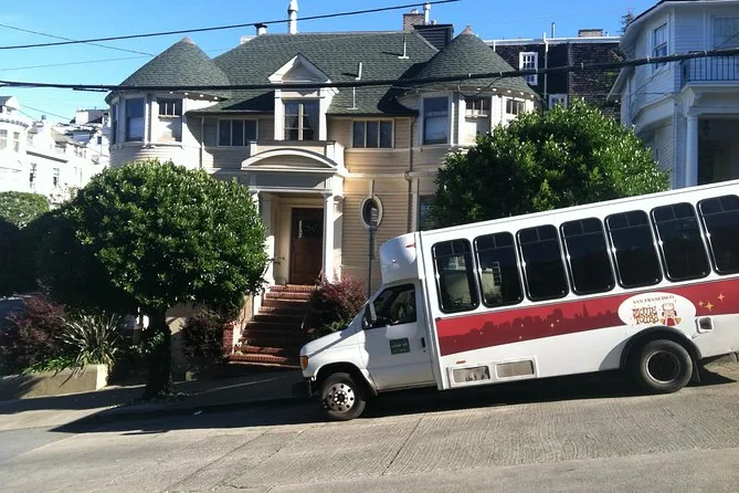A white tour minibus parked outside a large house on a residential street